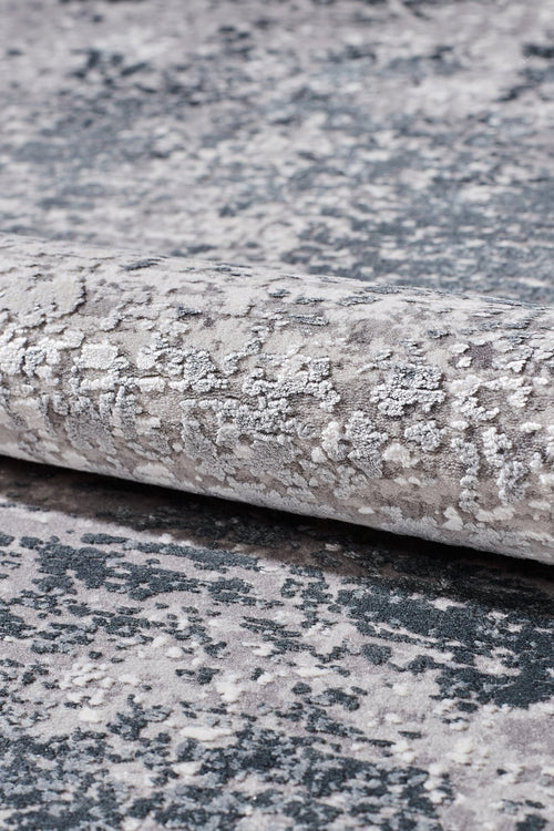 Load image 1 in gallery view. A close-up of the Vortexia Silver Premium Rug - M472A, showcasing its textured surface in gray, white, and dark blue with an abstract mottled design and subtle distressed details.