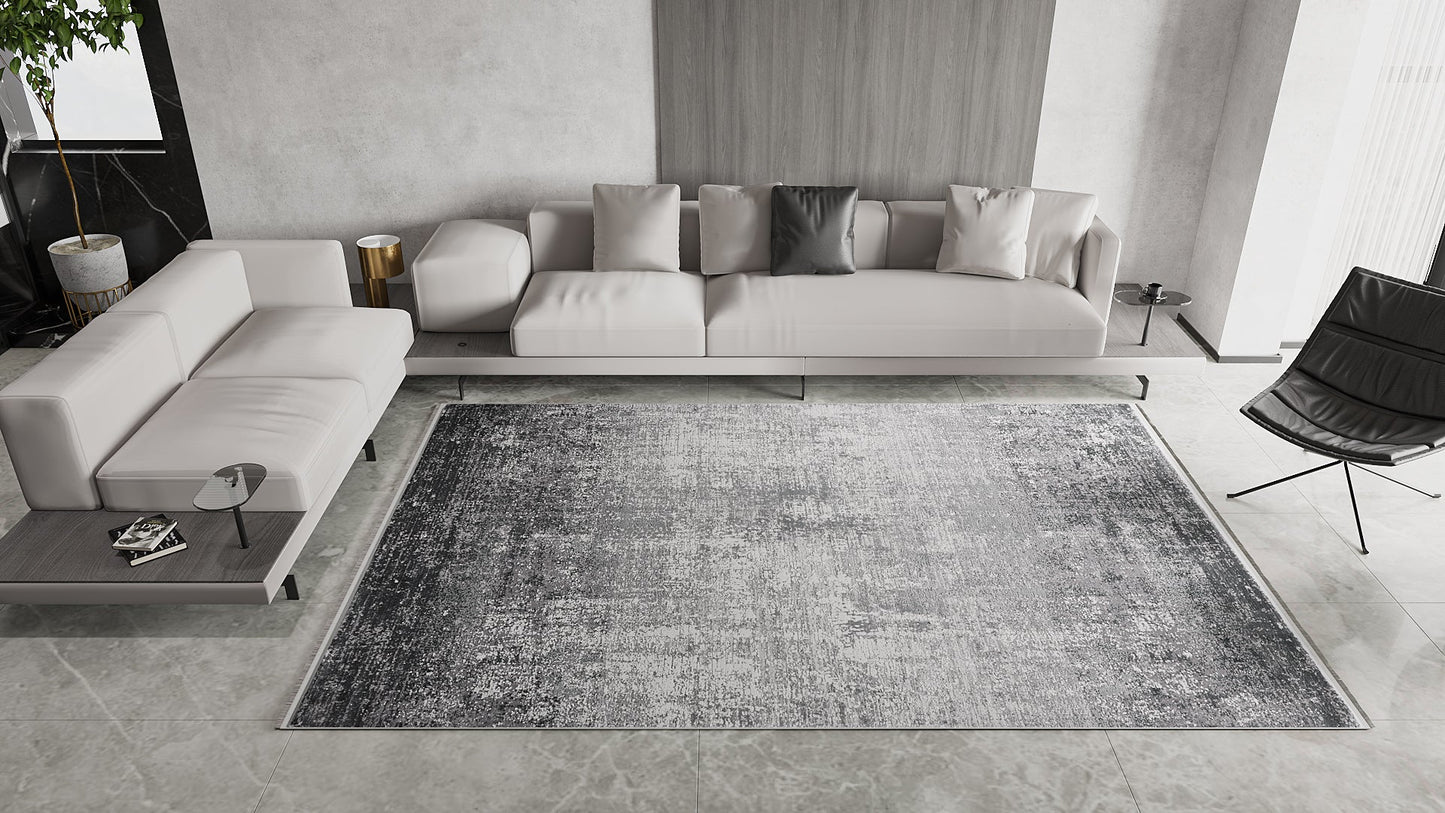 A modern living room featuring the Vortexia Silver Premium Rug - M472A, a light gray sectional with assorted cushions, a small side table, a black lounge chair, and minimalist neutral décor.