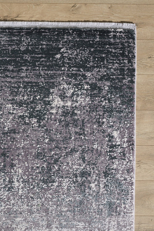 Load image 1 in gallery view. A close-up of the Vortexia Silver Premium Rug - M472A, a machine-made piece with a textured gray and purple mottled pattern and short white fringe, shown on a light wood floor.
