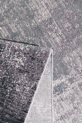 A close-up of the Vortexia Silver Premium Rug - M472A highlights its gray and purple tones, with one corner folded to reveal the lighter underside and intricate patterns on both sides.