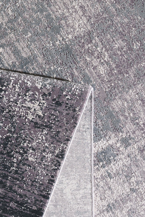 Load image 1 in gallery view. A close-up of the Vortexia Silver Premium Rug - M472A highlights its gray and purple tones, with one corner folded to reveal the lighter underside and intricate patterns on both sides.