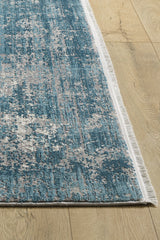 A close-up of the Vortexia Sky Premium Rug - M472B, a rectangular blue and white machine-made rug with white fringed edges and a textured abstract design, displayed on a light wood floor.