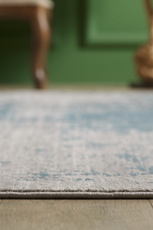 Load image 1 in gallery view. A close-up of the Vortexia Sky Premium Rug - M472B on a wooden floor, with a blurred chair and green wall in the background.