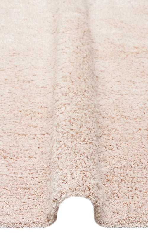 Load image 1 in gallery view. A close-up of the Warm Sand - Washable Shaggy - CBNPLAIN rug reveals its cream beige cotton texture, featuring a plush, fluffy surface and a raised, wave-like fold running vertically down the center.