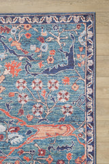 A corner of the Whisper Authentic Blue Washable Rug - LCC3034, featuring intricate floral and vine patterns in orange, red, and cream tones, is seen on a light wooden floor—ideal for high-traffic areas.