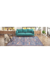 A modern living room features a teal sofa, the Whisper Authentic Blue Washable Rug (LCC3034), ideal for high-traffic areas, a wooden chair with a beige throw, and plants on a wooden shelf below windows.