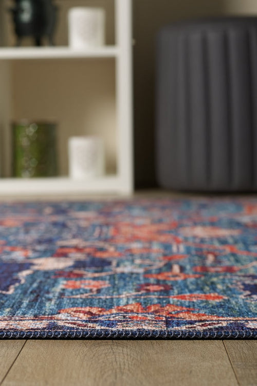 Load image 1 in gallery view. A close-up of the Whisper Authentic Blue Washable Rug - LCC3034 (Custom Size) on a wooden floor, with a white shelf and gray ottoman behind it. The shelf holds a green glass and two white textured containers—ideal for high-traffic areas.