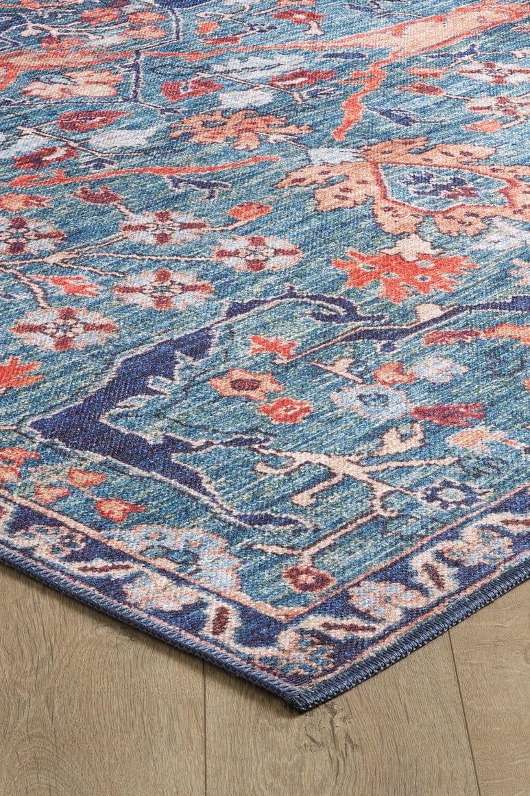 A close-up of the Whisper Authentic Blue Washable Rug - LCC3034 (Custom Size) featuring vibrant orange and cream floral patterns with a decorative border, shown on a light wooden floor—ideal for high-traffic areas.