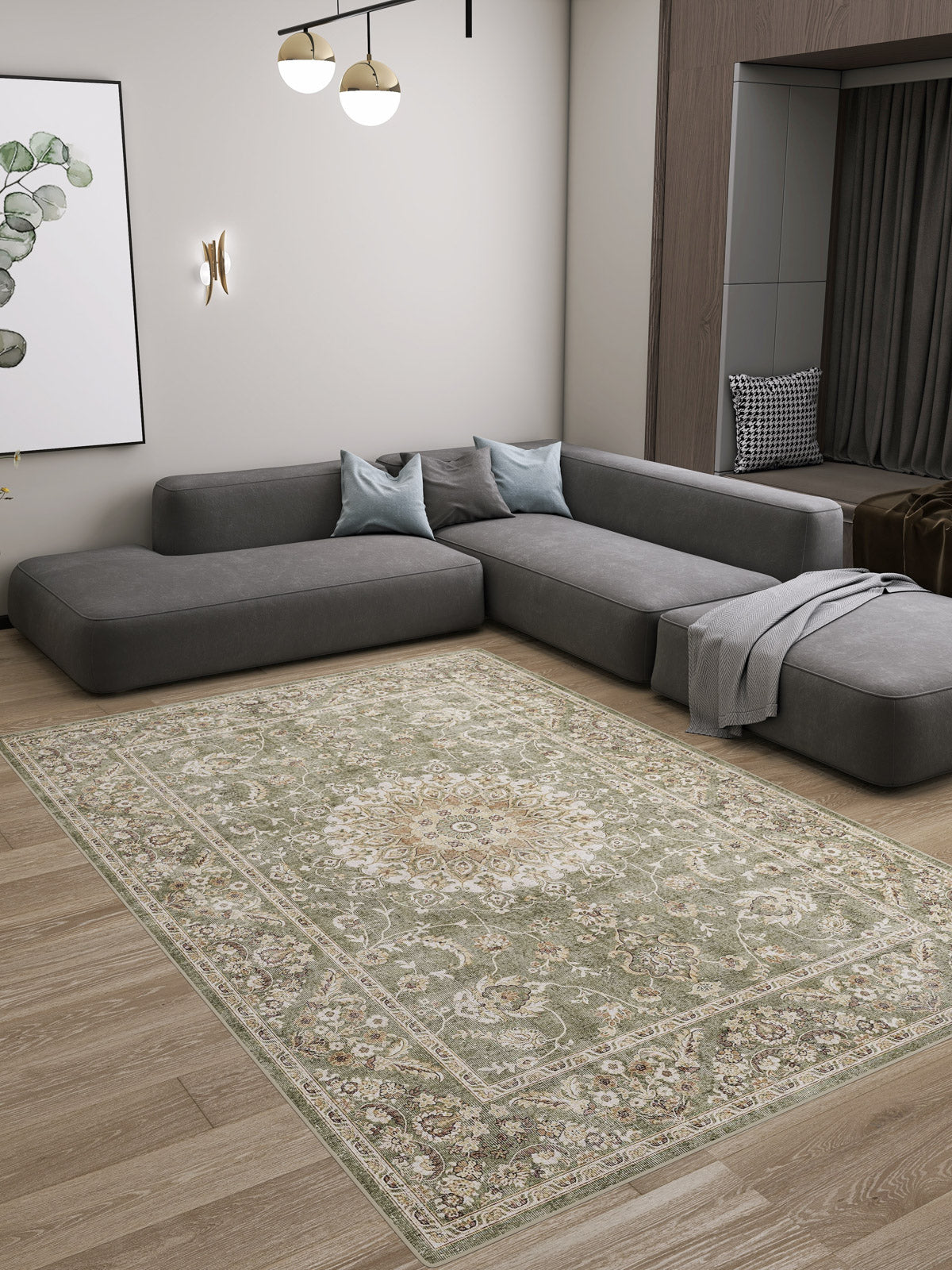 A modern living room features a large gray sectional, light blue cushions, a throw blanket, and the Whispered Heritage - Washable Rug - JRN30 on wooden floors. Minimalist decor includes wall art, a sconce, and pendant lighting.