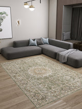 A modern living room features a large gray sectional, light blue cushions, a throw blanket, and the Whispered Heritage - Washable Rug - JRN30 on wooden floors. Minimalist decor includes wall art, a sconce, and pendant lighting.