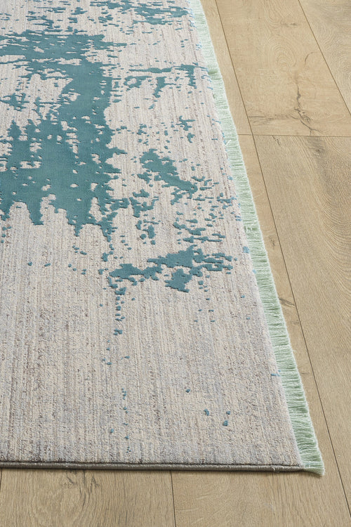 Load image 1 in gallery view. The Whispering Mist Modern Rug - Blue - HRD001, a machine-made rug with teal abstract patterns and a textured, fringed design, lies partly out of the image frame on a wooden floor.