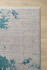 The Whispering Mist Modern Rug - Blue - HRD001, a machine-made rug with teal and beige abstract patterns and fringe tassels, adds a stylish, distressed look to any contemporary space on light wooden floors.