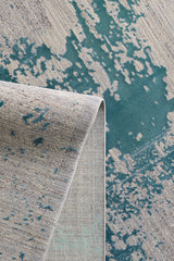 A close-up of the Whispering Mist Modern Rug - Blue - HRD001 shows its folded corner, abstract teal and beige pattern, and subtle stitching on the underside, highlighting the rug’s unique modern distressed texture and design.
