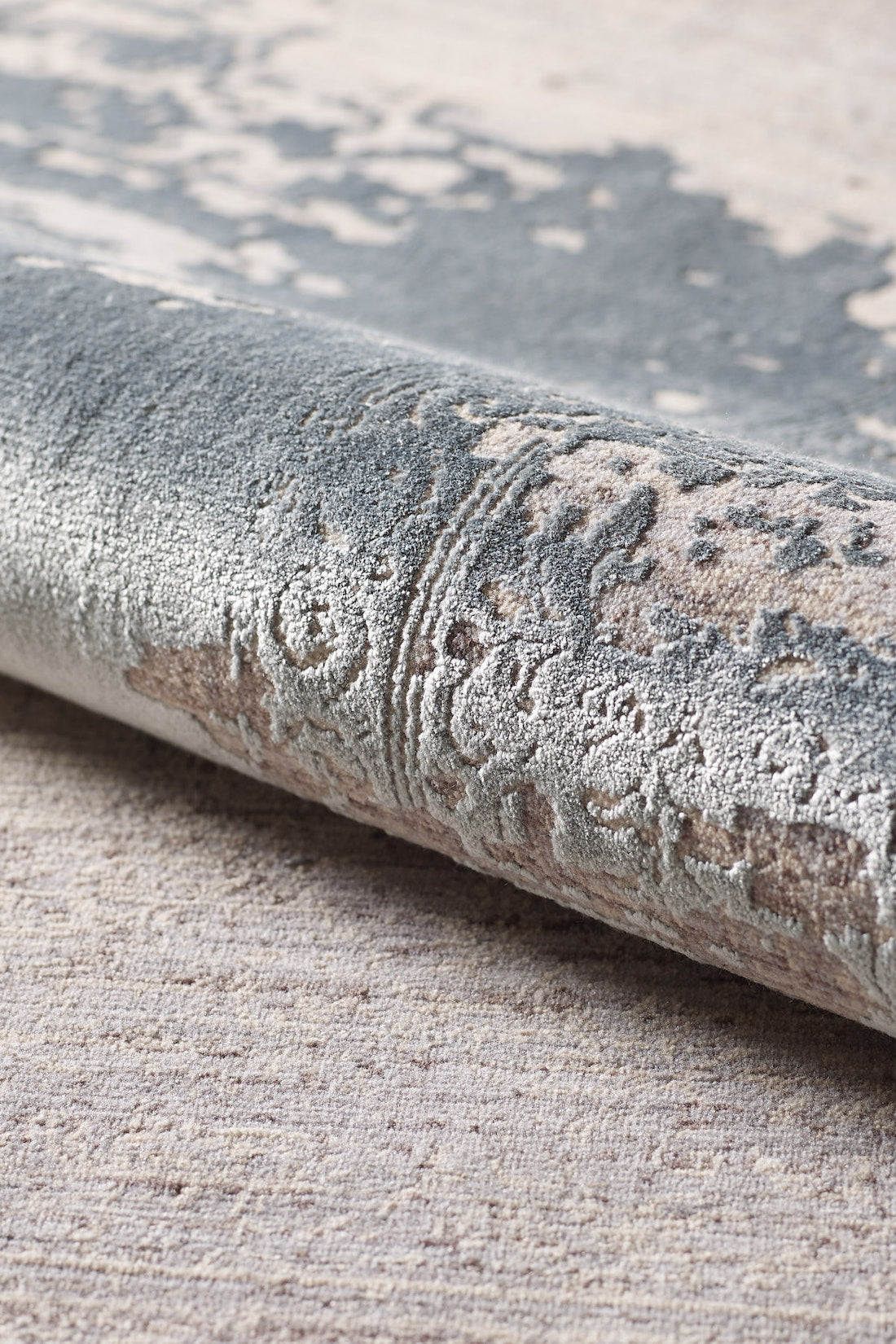 A close-up of the Whispering Mist Modern Rug - Silver - HRD002 highlights its machine-made, rolled edge with intricate gray, beige, and cream patterns plus a soft, plush surface for a modern distressed look.