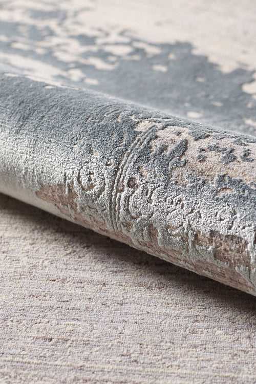 Load image 1 in gallery view. A close-up of the Whispering Mist Modern Rug - Silver - HRD002 highlights its machine-made, rolled edge with intricate gray, beige, and cream patterns plus a soft, plush surface for a modern distressed look.