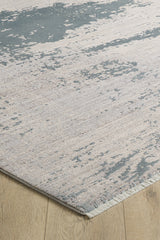 A close-up of the Whispering Mist Modern Rug - Silver (HRD002) shows its abstract beige pattern on a light wood floor. This machine-made rug has visible edging and a modern, slightly distressed, worn look.