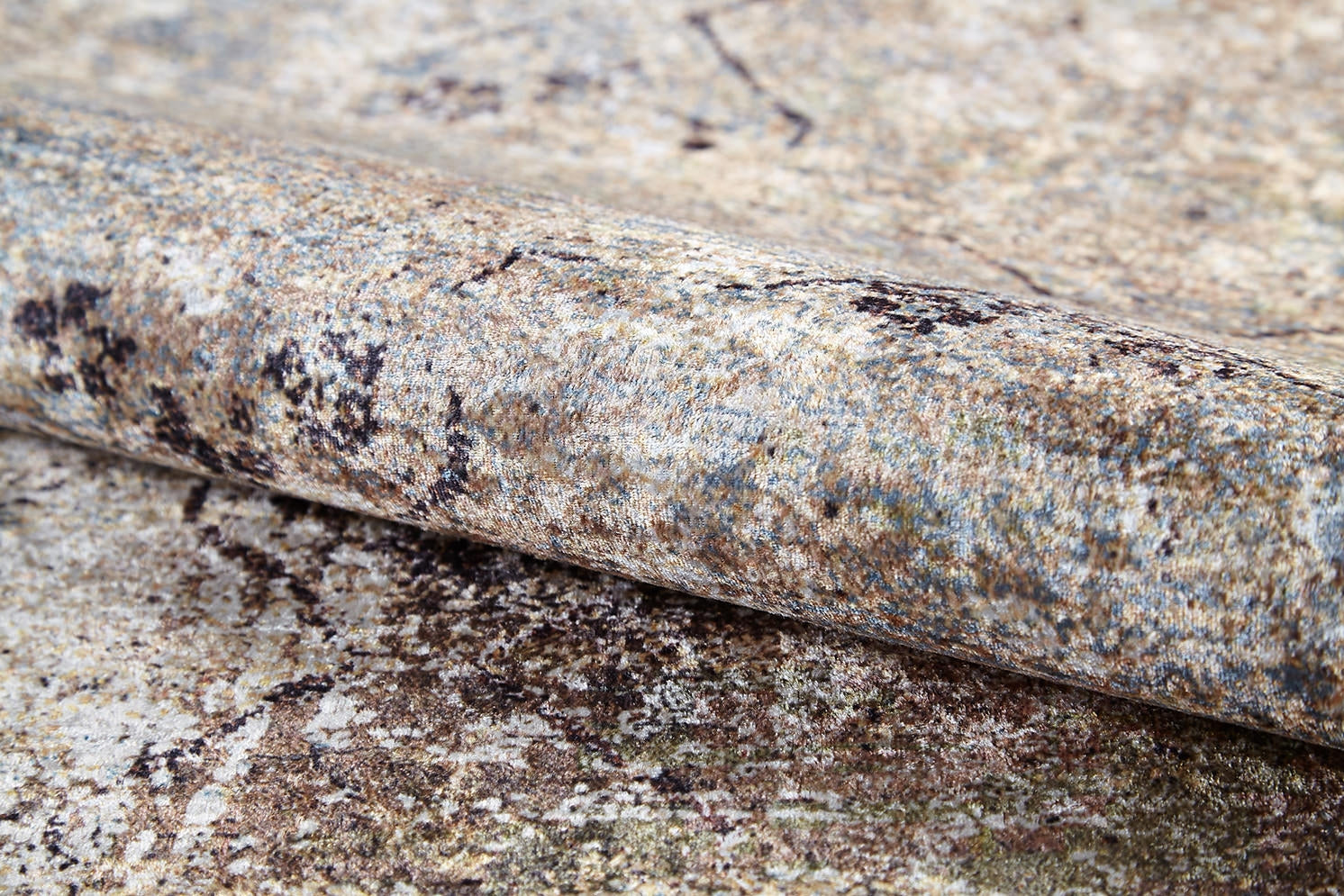 A close-up of the Windowpane Trellis - Washable Rug - JR1663 (Custom Size) shows its weathered, rolled-up form and rough, speckled surface with bronze and brown shades, highlighting the rug’s natural textures and patterns.