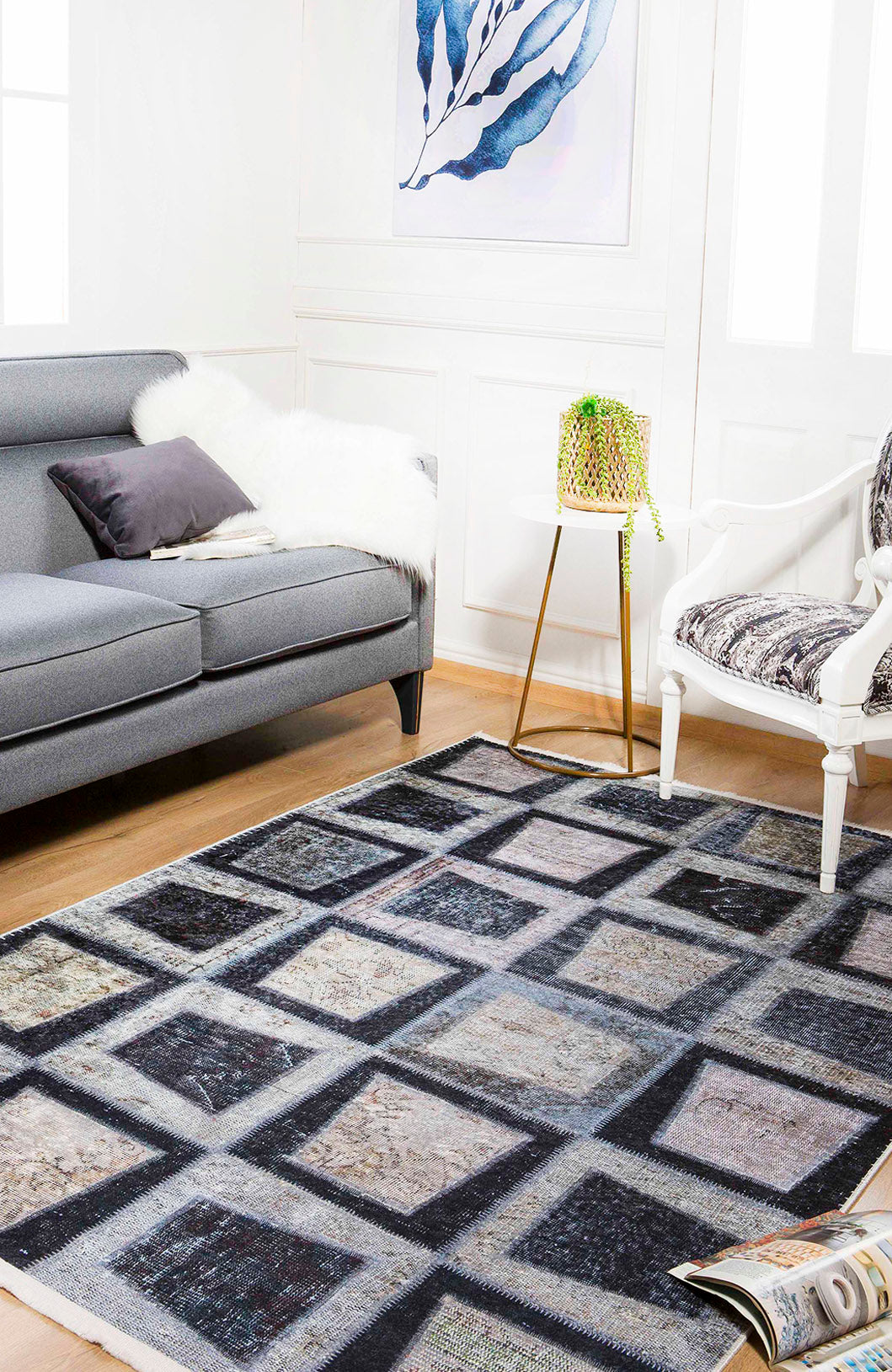 A modern living room with a gray sofa, white armchair, Windowpane Wonder - Washable Rug - JR184 (Custom Size) ideal for high-traffic areas, small side table with a plant, fur throw, framed leaf artwork, and an open magazine on the floor.