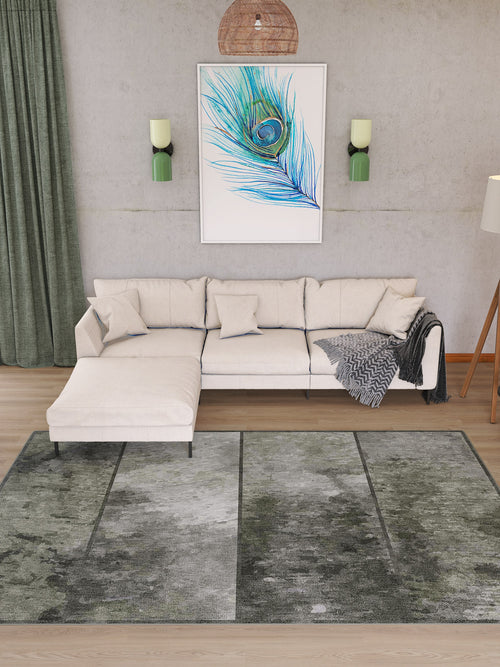 Load image 1 in gallery view. A modern living room featuring a light beige sectional sofa, green curtains, two wall sconces, a cozy throw blanket, a framed peacock feather print, and the Wistful Pattern - Washable Rug - JRN35 (Custom Size) in greenish-gray patterns.