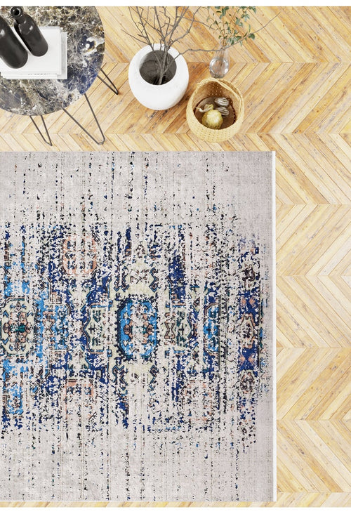 Load image 1 in gallery view. A top-down view of the Worn-Out Abstract - Washable Rug - JR339 on herringbone wood flooring, by a small table, white vase with branches, and wicker basket—ideal for high-traffic and allergy-sensitive spaces.
