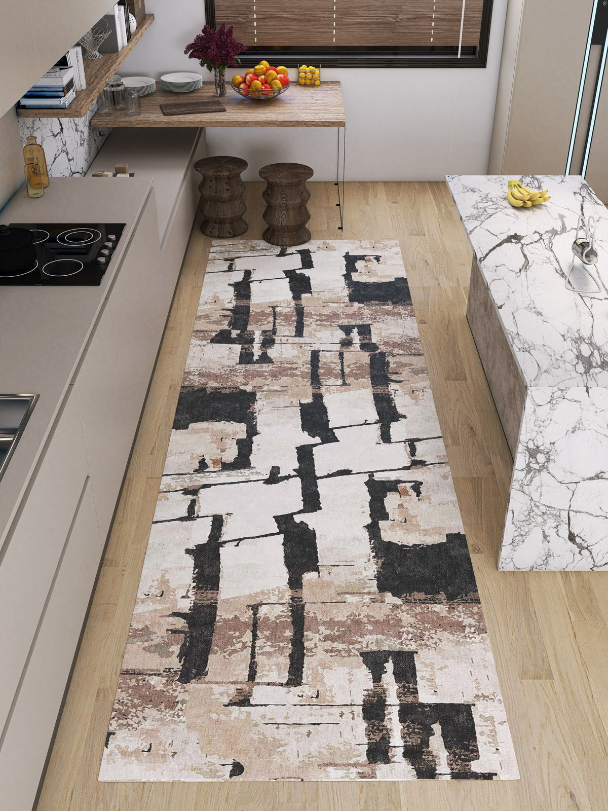 A modern kitchen with light wood floors, a marble island, minimalist beige cabinets, and a Woven Memoir - Washable Rug - JRN41 in cream, brown, and black running alongside the counters. A table with stools and fruit sits in the background.