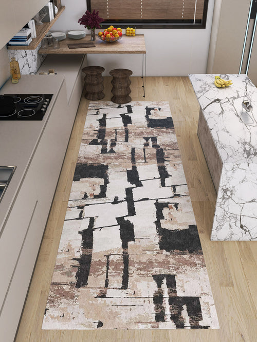 Load image 1 in gallery view. A modern kitchen with light wood floors, a marble island, minimalist beige cabinets, and a Woven Memoir - Washable Rug - JRN41 in cream, brown, and black running alongside the counters. A table with stools and fruit sits in the background.