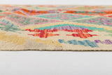 Close-up side view of the Woven Nomad - Handwoven Kilim, a vibrant flatweave rug with geometric patterns in red, blue, green, yellow, and orange on a cream background, displayed on a white surface.