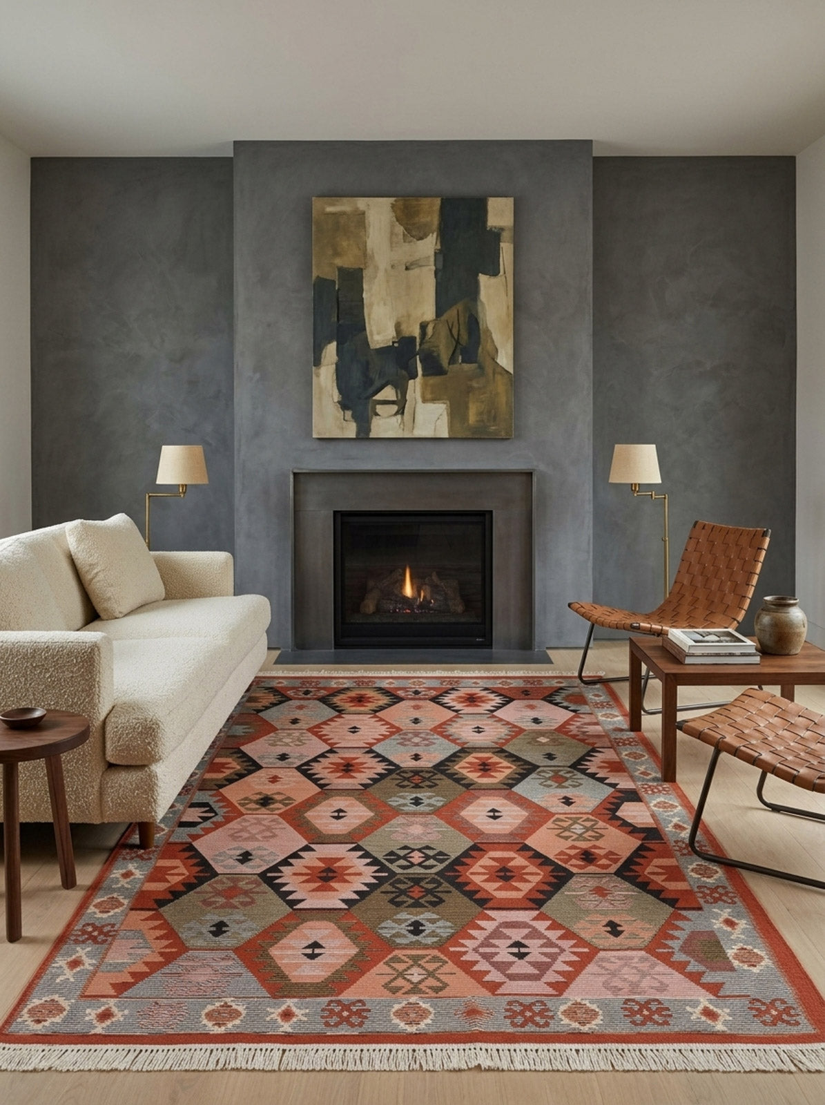 A modern living room with a beige sofa, two woven leather chairs, the Woven Spirit - Washable Reversible Kilims - AR42 rug, a lit fireplace, abstract art above the mantle, and two lamps against a gray accent wall.