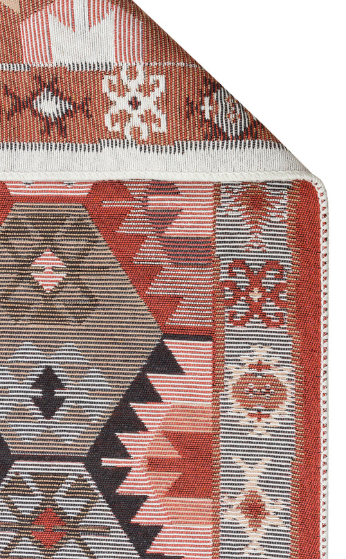 Load image 1 in gallery view. A close-up of the Woven Spirit - Washable Double-Sided Kilims - AR42 shows vibrant red, brown, pink, and white geometric patterns on recycled cotton with a folded corner and white-stitched edge.