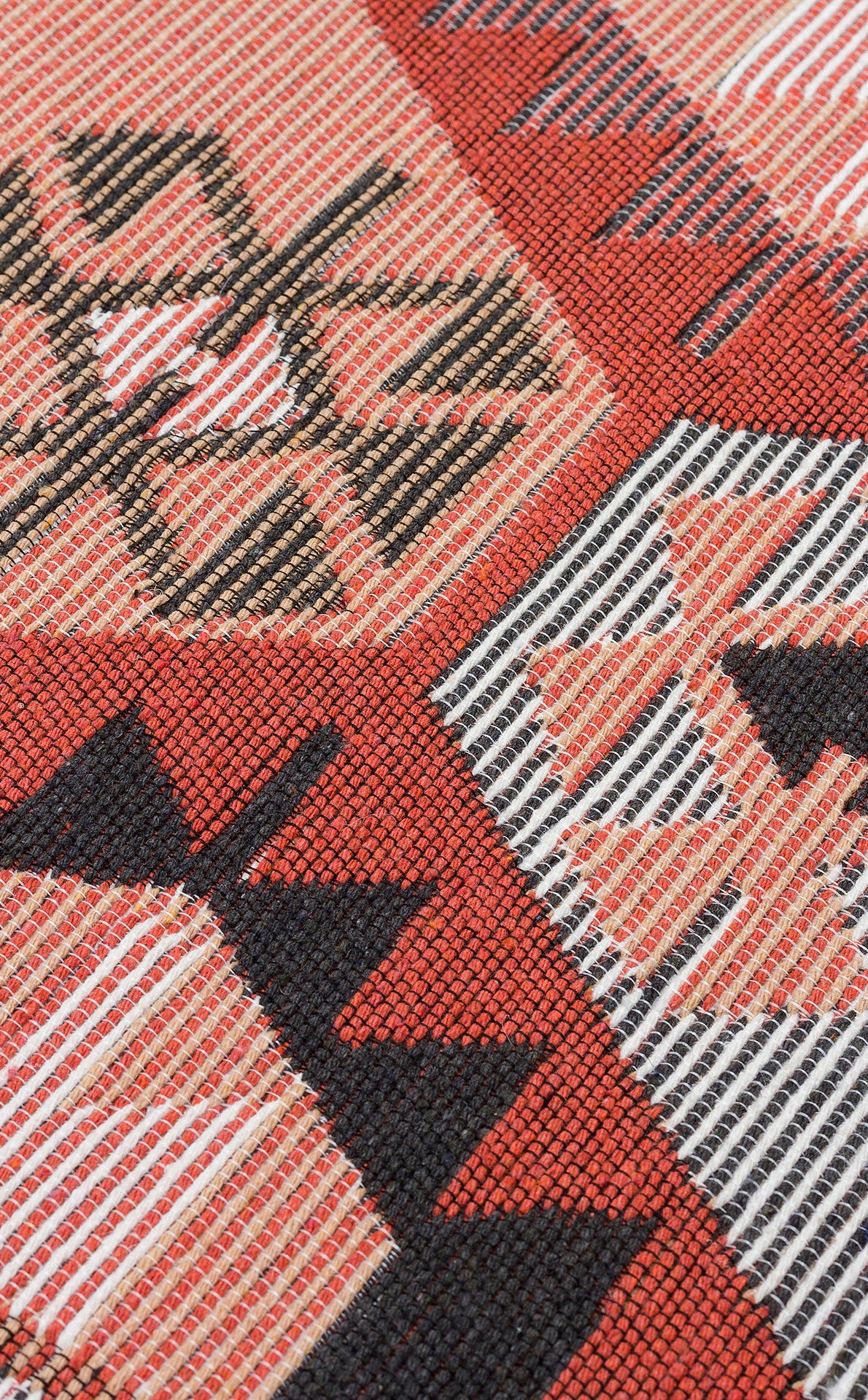 Close-up of the Woven Spirit - Washable Double-Sided Kilims - AR42, highlighting geometric patterns in red, black, white, and tan with intersecting lines, triangles, and diamonds. The textile's fine texture and threads are clearly visible.