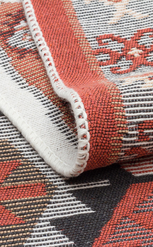 Load image 1 in gallery view. Close-up of the Woven Spirit - Washable Double-Sided Kilims - AR42 with a folded corner, highlighting detailed stitching, colorful red, white, brown, and black patterns, plus the visible texture and intricate design.