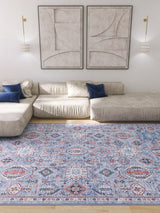 A modern living room with a cream sectional, blue accent pillows, abstract wall art, wall-mounted lights, and the Xanadu Handmade-Design Blue Washable Rug (LCC3013) featuring red and white patterns—ideal for high-traffic wooden floors.