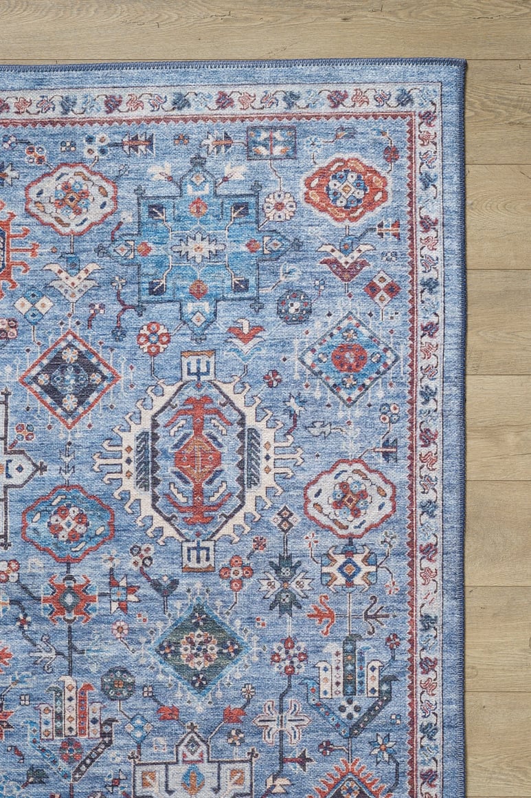 The Xanadu Handmade-Design Blue Washable Rug (LCC3013) with geometric and floral red, white, and navy accents is shown partially on a light wood floor, highlighting its durability for high-traffic areas.