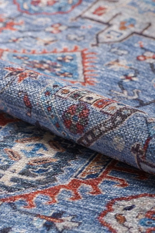 Bild 1 in Galerieansicht laden. A close-up of the Xanadu Handmade-Design Blue Washable Rug – LCC3013, rolled to reveal its intricate red, white, and dark blue patterns with traditional motifs—perfect for adding style to high-traffic areas and easy to clean.