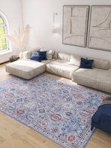 A bright living room with a beige sectional sofa, blue accent pillows, textured wall art, a Xanadu Handmade-Design Blue Washable Rug - LCC3013 (Custom Size) featuring red patterns, light wood floor, and a sunlit window.