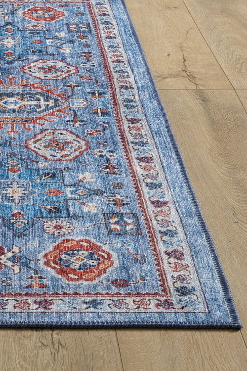 Bild 1 in Galerieansicht laden. A corner of the Xanadu Handmade-Design Blue Washable Rug - LCC3013, featuring intricate red, white, and light blue geometric patterns, is shown on a light wood floor. Only part of this custom-size flat weave rug is visible in the image.