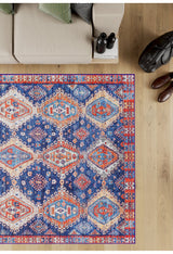 The Zephyro Kilim-Design Washable Rug - LCC3008 (Custom Size) with vibrant geometric patterns lies on a wooden floor by a beige sofa with green cushions—ideal for allergy-sensitive, high-traffic homes. Nearby: black bag, two bottles, brown shoes.