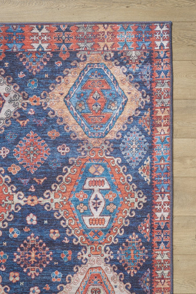 A corner of the Zephyro Kilim-Design Washable Rug - LCC3008 (Custom Size), featuring red, blue, white, and orange geometric and diamond patterns, lies on a light wood floor—ideal for high-traffic areas.
