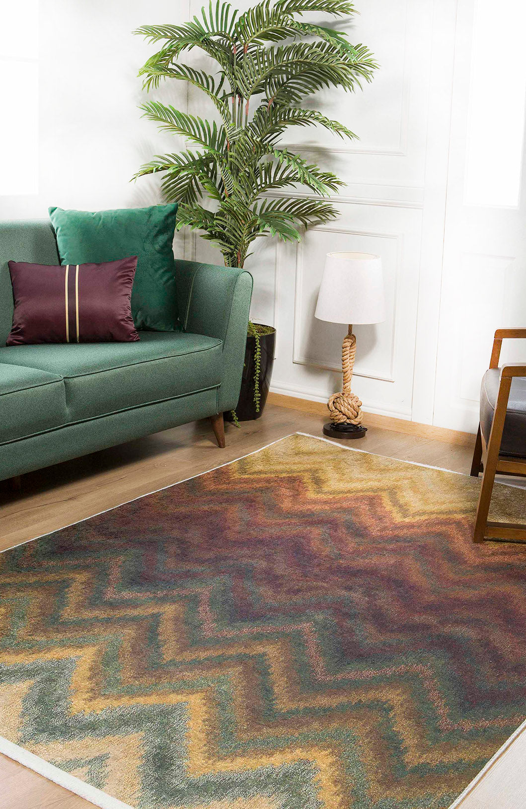 A cozy living room with a green sofa, purple cushion, potted plant, rope-base lamp, and the Zigzag Runway - Washable Rug - JR388 (Custom Size), perfect for high-traffic wooden floors with its multicolor zigzag pattern.