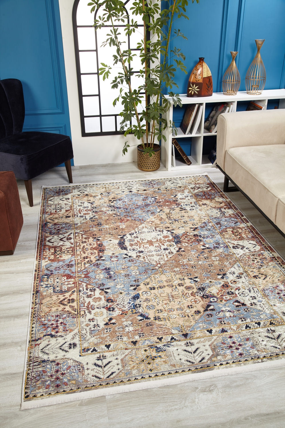 The Native Nature's Washable Rug - JR1666 (Custom Size) with vibrant geometric and floral patterns adds style to a modern living room with a beige sofa, black chair, tall plant, and blue paneled walls—ideal for high-traffic areas.