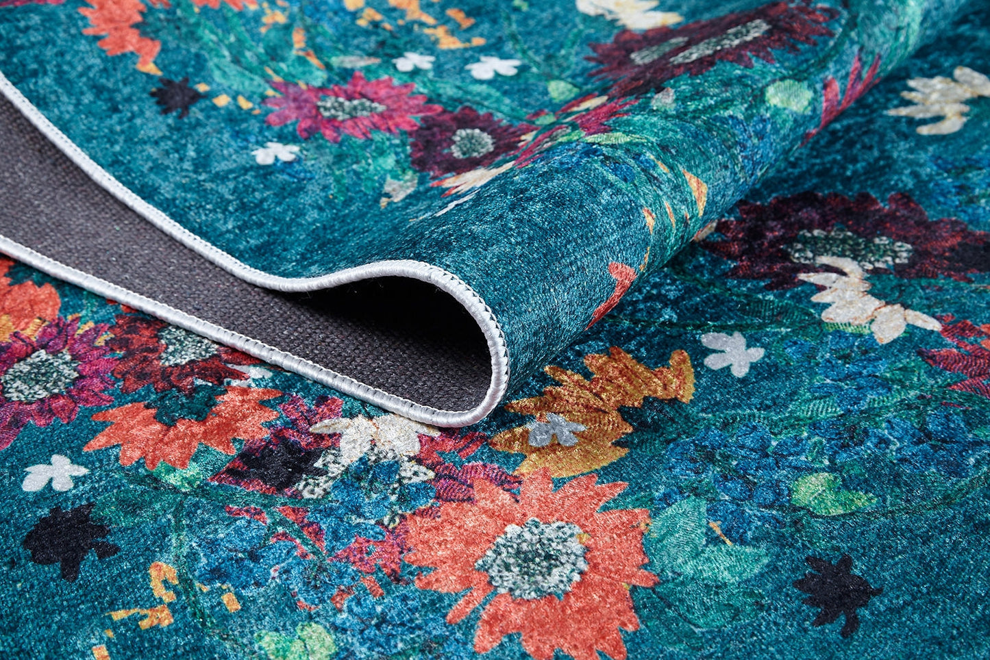 Close-up of Nature's Tapestry - Washable Rug - JR1674 (Custom Size): a vibrant, multi-colored floral rug with a teal background. The folded corner shows its textured, non-slip gray backing and sturdy edge stitching—ideal for high-traffic areas.