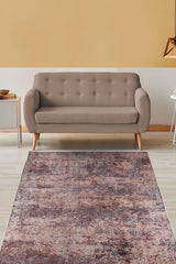 A modern living room features a beige sofa, small white side table, and the Abstract Spectrum - Washable Rug - JR1427 in bronze, brown, and mauve tones on light wood floors—ideal for allergy-sensitive homes—set against a yellow accent wall.