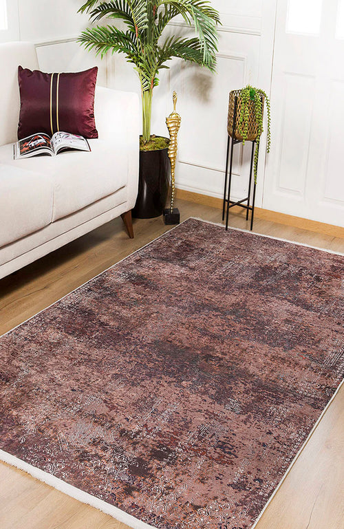 Load image 1 in gallery view. A modern living room with a beige sofa, burgundy pillow, open book, potted plant, gold statue, and the Abstract Spectrum - Washable Rug - JR1427 in bronze and brown on wooden floors. Sunlight streams through white doors.