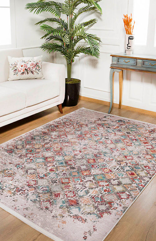 Load image 1 in gallery view. A living room with a beige sofa, floral pillow, large plant, and blue console table features the Aged Mosaic - Washable Rug - JR1096 for vibrant color on the wooden floor, while orange flowers in a vase brighten the console.