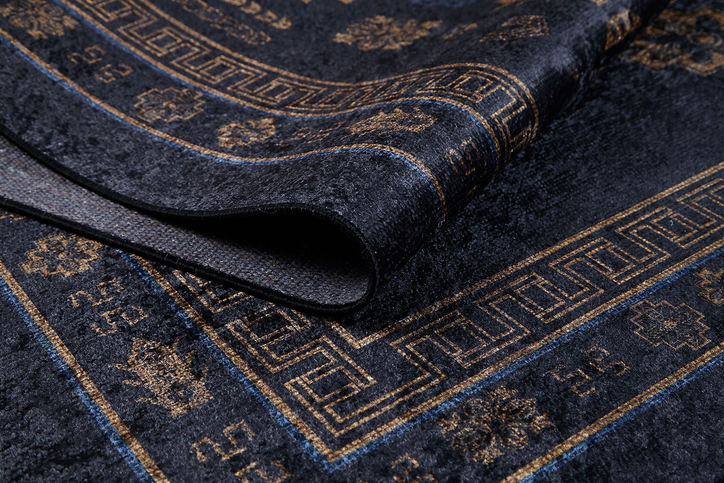 A close-up of the Ancient Legacy - Washable Rug - JR1890, in dark blue with gold geometric and floral patterns, partially folded to highlight its texture—an ideal washable rug for high-traffic spaces.