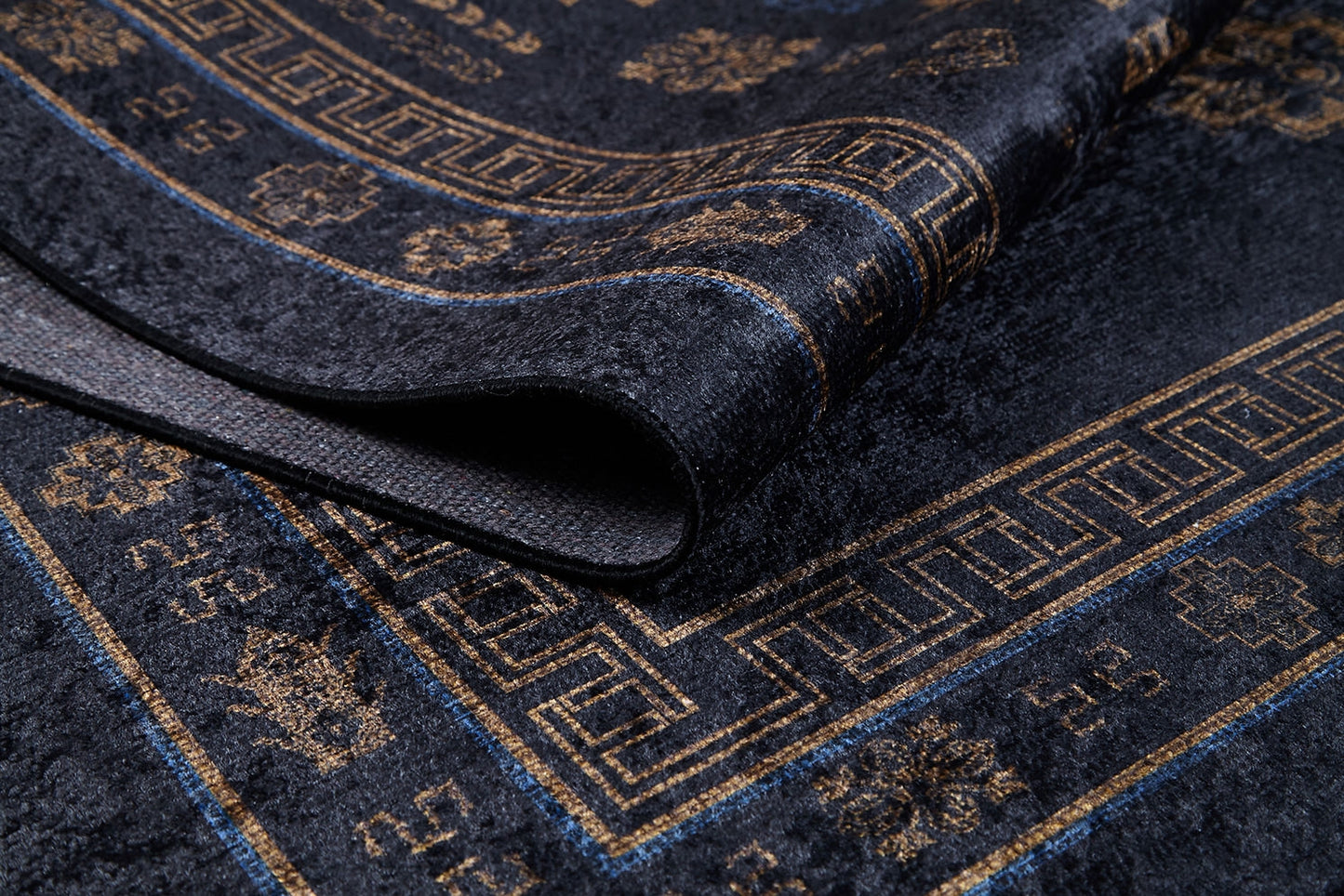 A close-up of the Ancient Legacy - Washable Rug - JR1890, in dark blue with gold geometric and floral patterns, partially folded to highlight its texture—an ideal washable rug for high-traffic spaces.