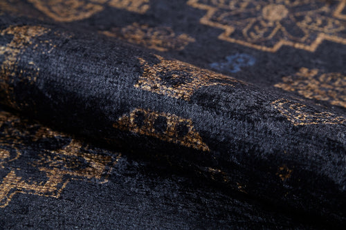 Load image 1 in gallery view. A close-up of the Ancient Legacy - Washable Rug - JR1890, showcasing its dark, plush fabric and intricate golden-brown floral and geometric pattern with a rolled edge to highlight texture—ideal for high-traffic areas.