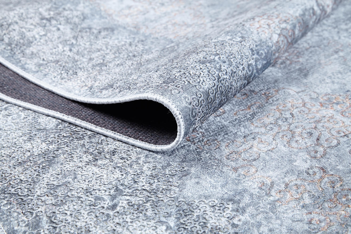 A close-up of the Ancient Treasure - Washable Rug (JR1785) in gray displays its intricate patterns and lifted edge, revealing the textured underside—ideal for high-traffic spaces.