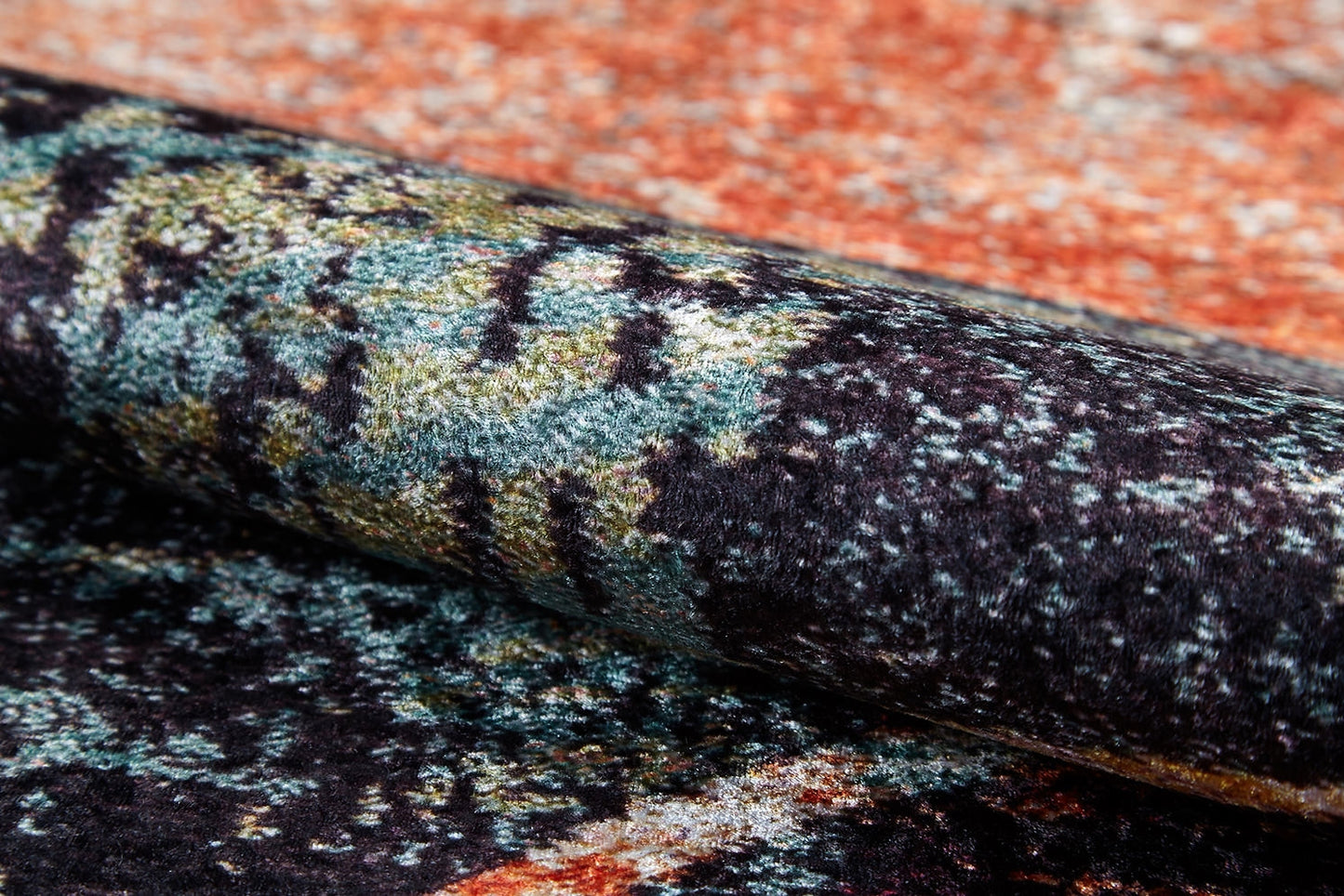 A close-up of the Angular Beauty - Washable Rug (JR2002), featuring a rolled, textured surface with an abstract pattern in black, green, yellow, orange, and blue. Its soft, plush fabric is ideal for high-traffic areas and easy to clean.