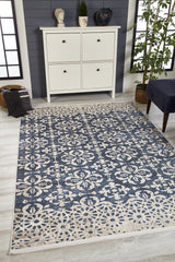 The Antique Flourish - Washable Rug - JR1591, featuring blue and beige floral patterns, adds style to a modern room with a white cabinet, potted plant, navy chair, and décor—ideal for high-traffic areas with large windows and a dark accent wall.